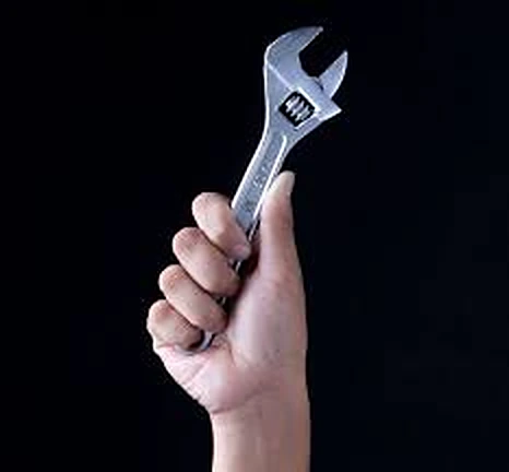 A hand holding up an adjustable wrench against a black background